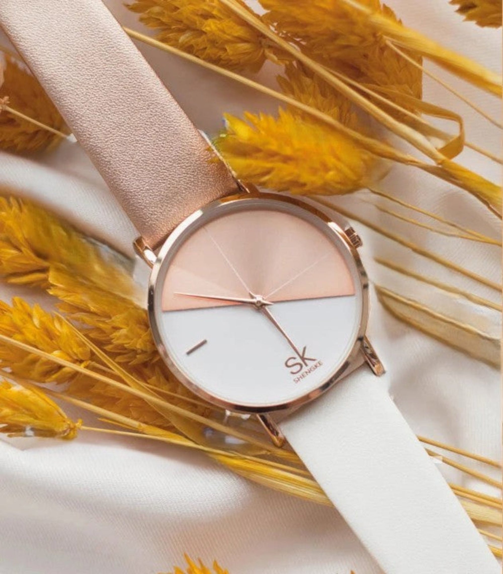 Watch with a white strap and rose gold case on a background of yellow dried flowers