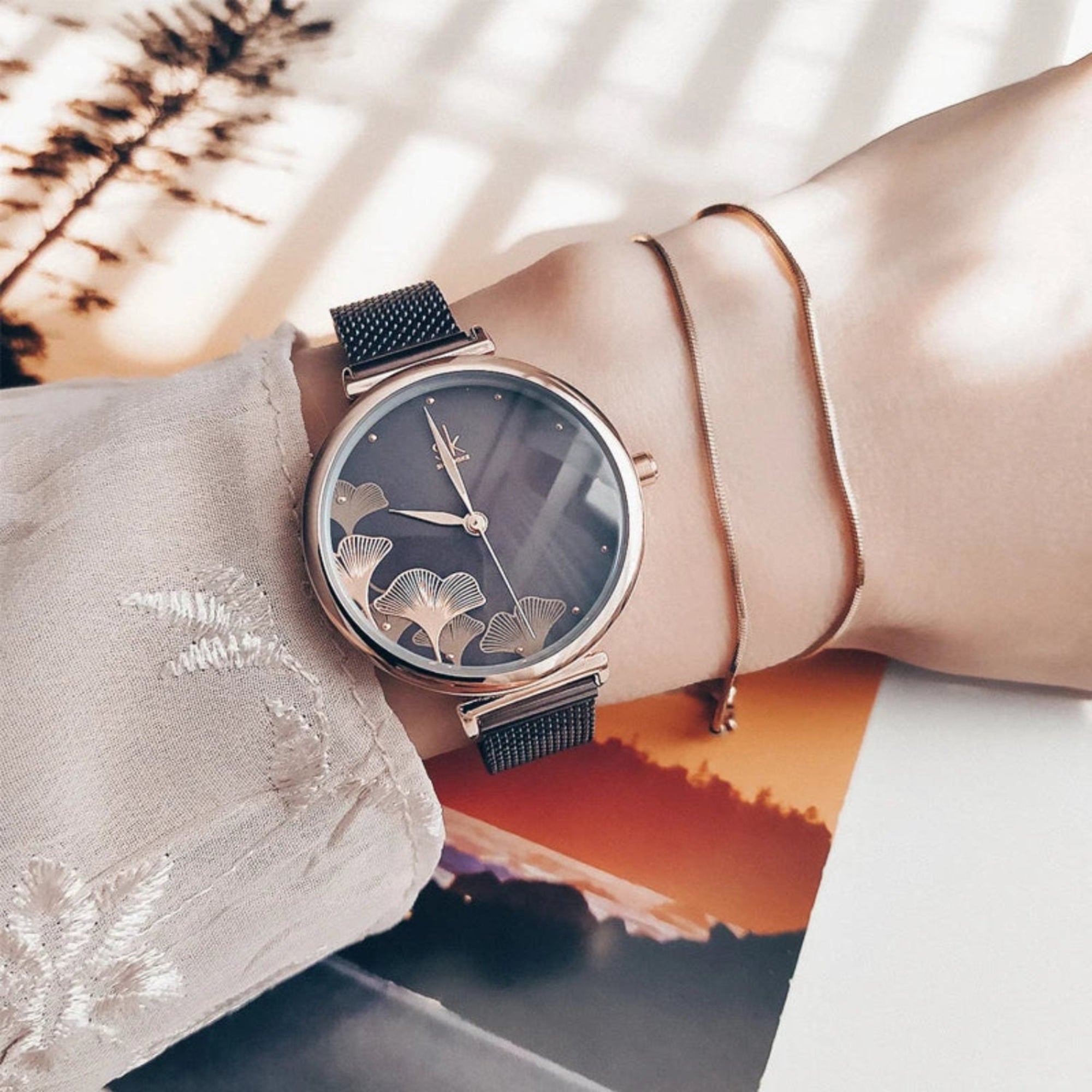 Rose gold watch with black strap on a wrist against a blurred natural background