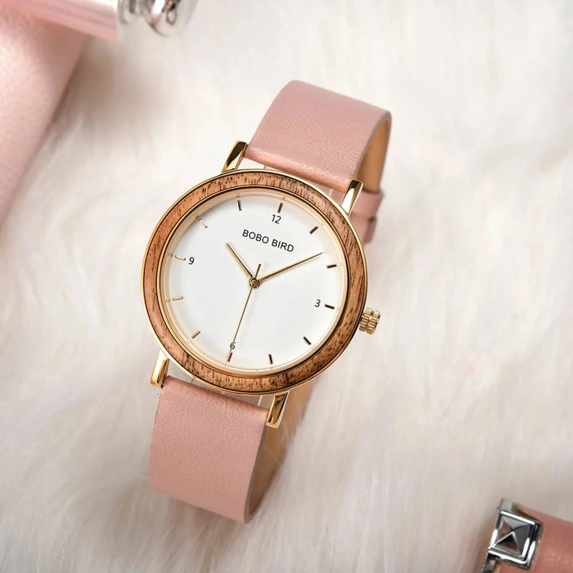 A BoBo Bird women's watch with a pink leather band and a gold-colored case, displayed on a white furry surface.