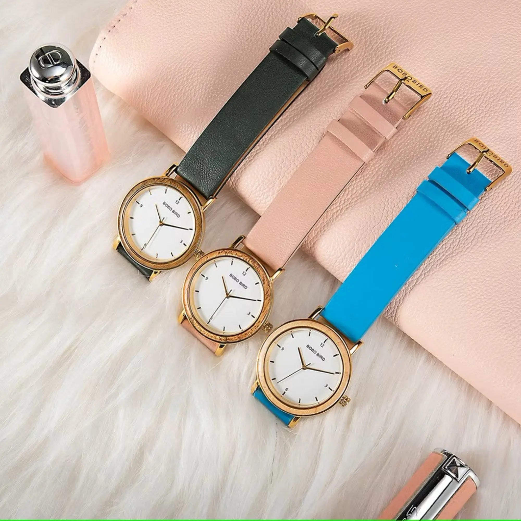 Three watches with different colored straps on a light wooden surface.