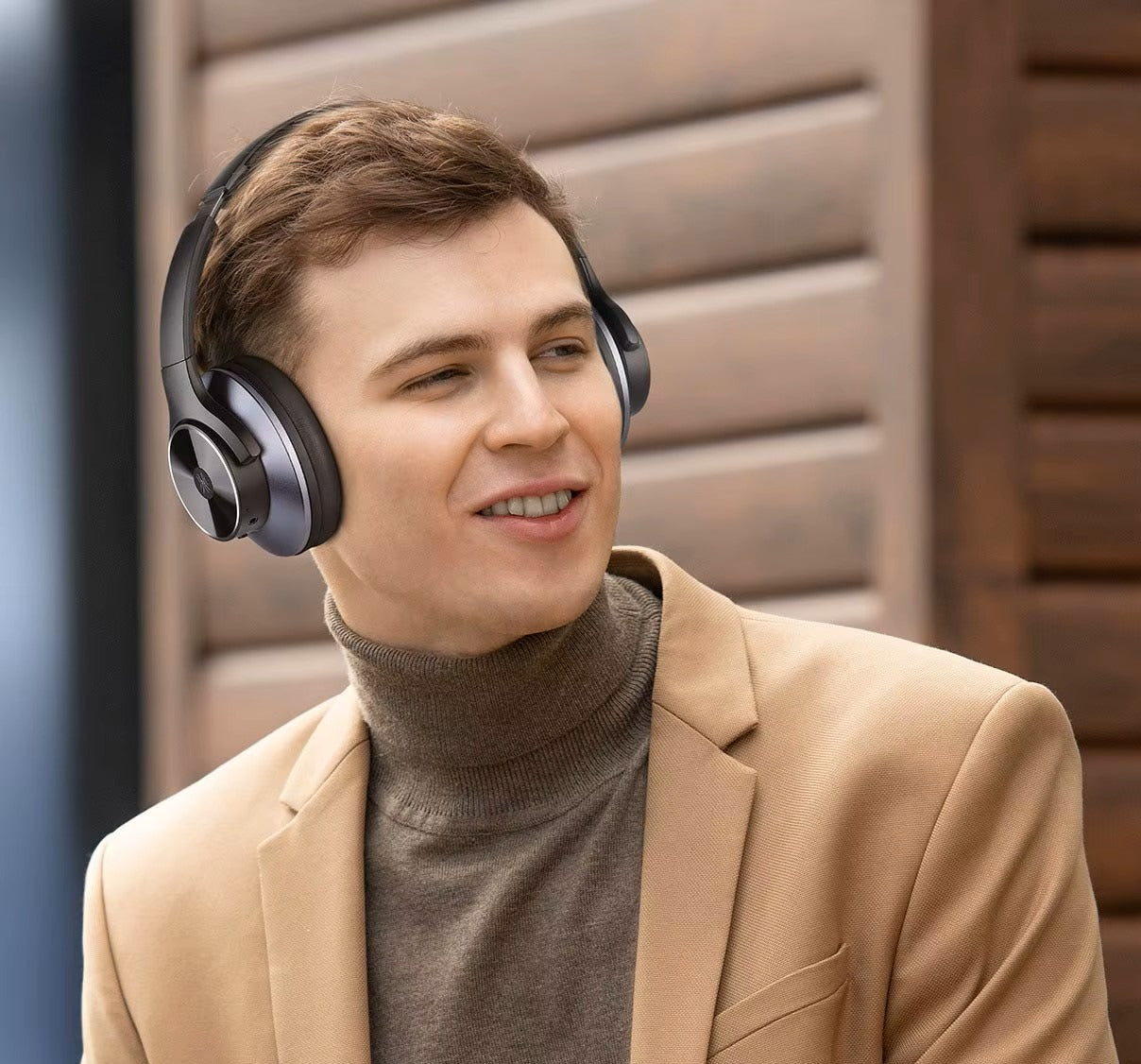 Man wearing headphones and a beige blazer with a brown turtleneck sweater.