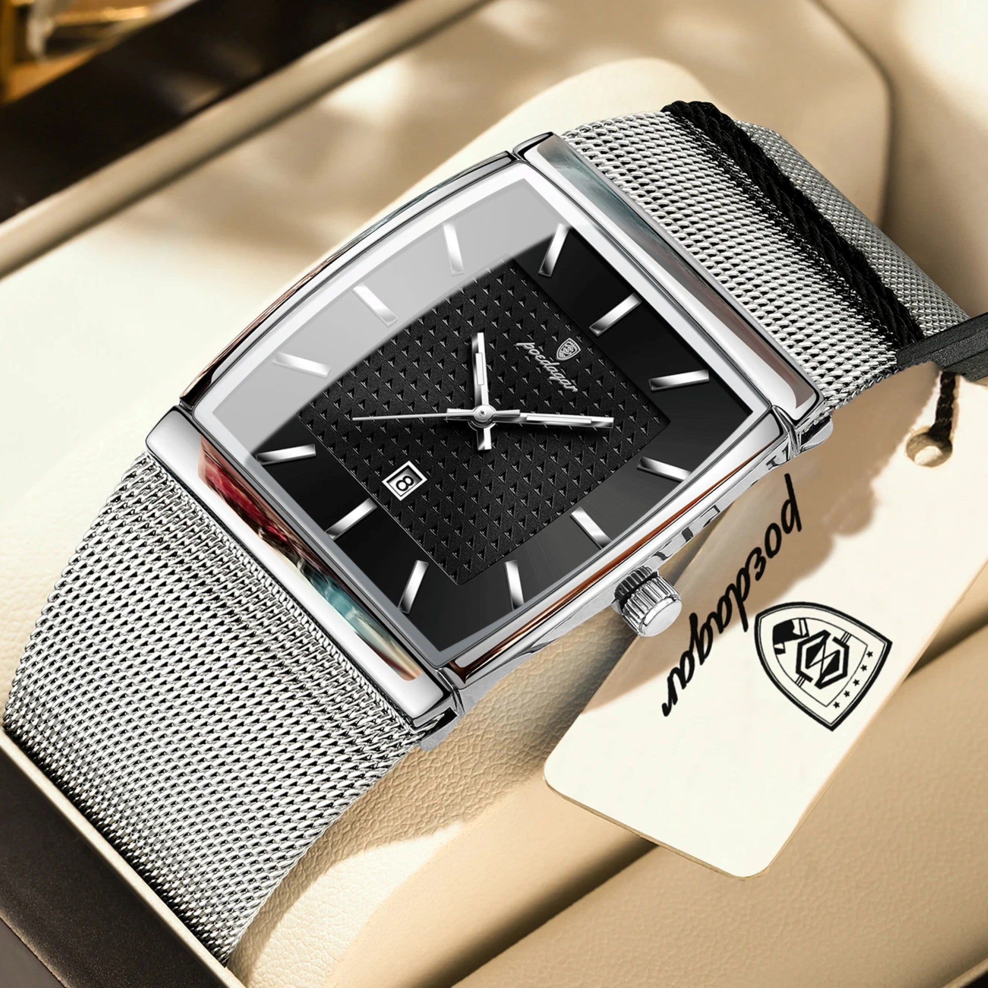 Silver watch with black face on a beige surface, featuring a brand tag.