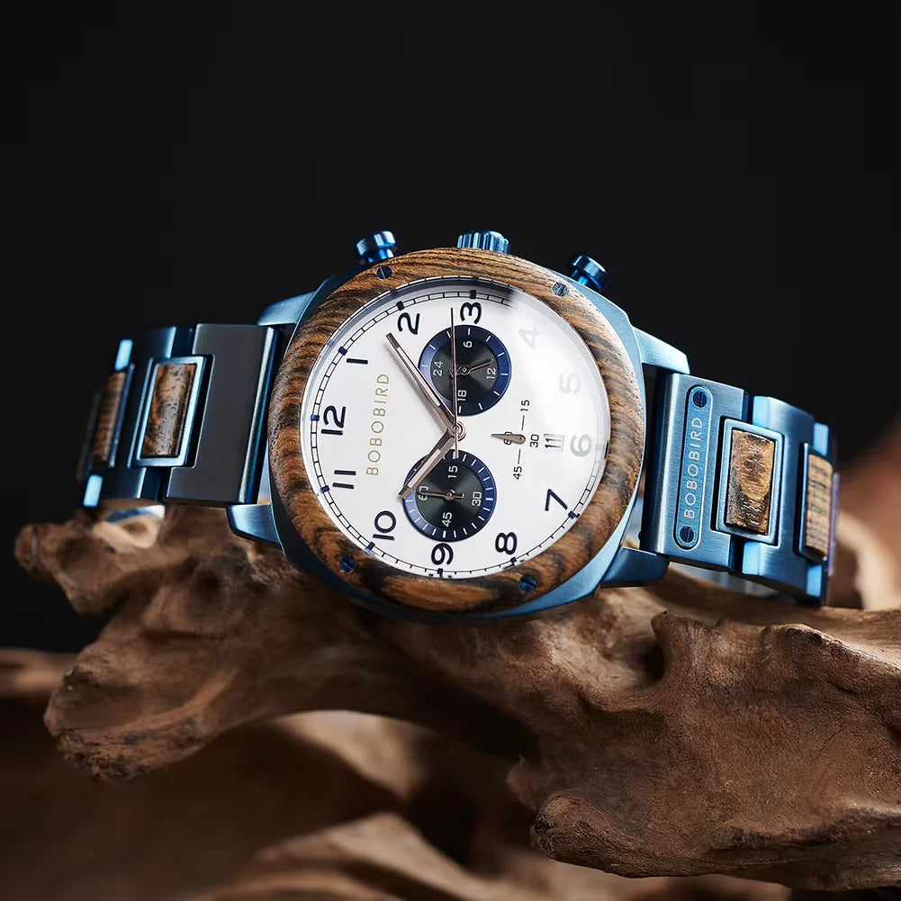 Boboiprin men's watch with a blue stainless steel case and link bracelet featuring wood inlays, a white dial with black numerals, and two blue subdials, displayed on a piece of driftwood against a dark background.