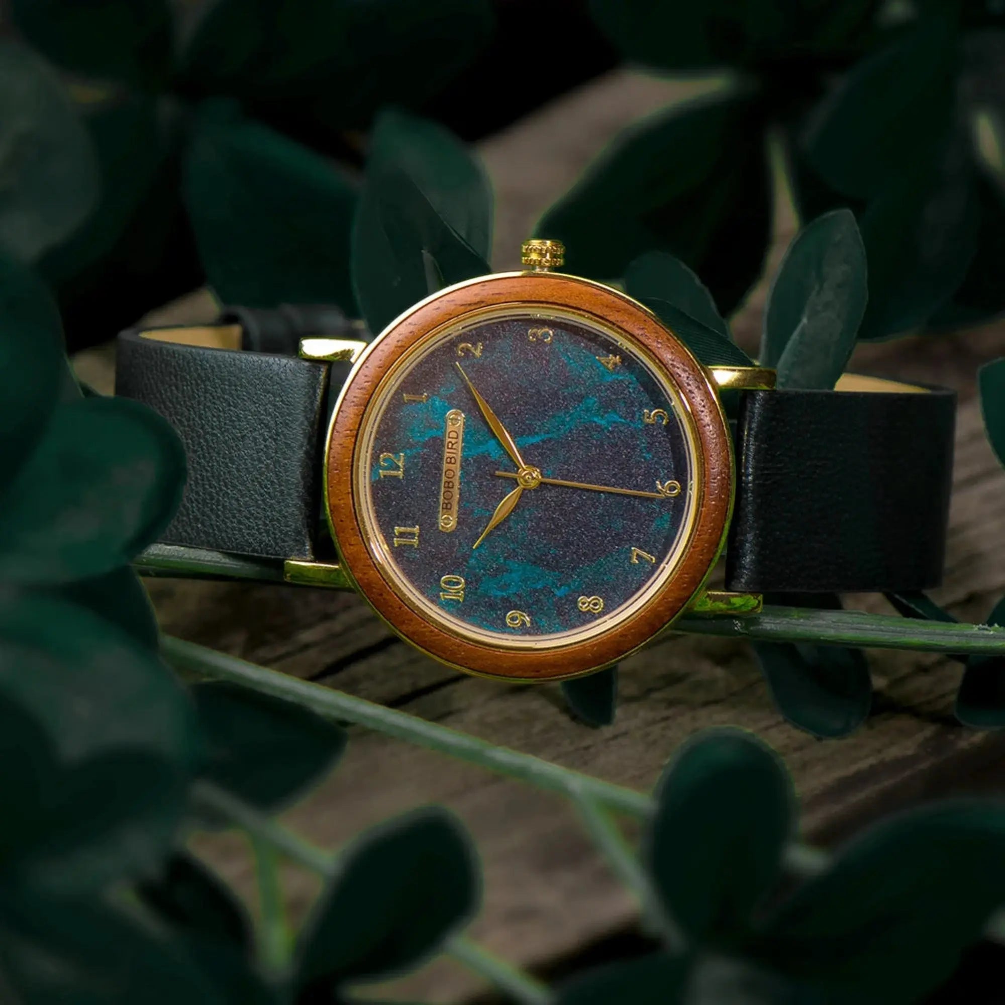 Wristwatch with a blue and gold face and black strap on a leafy background