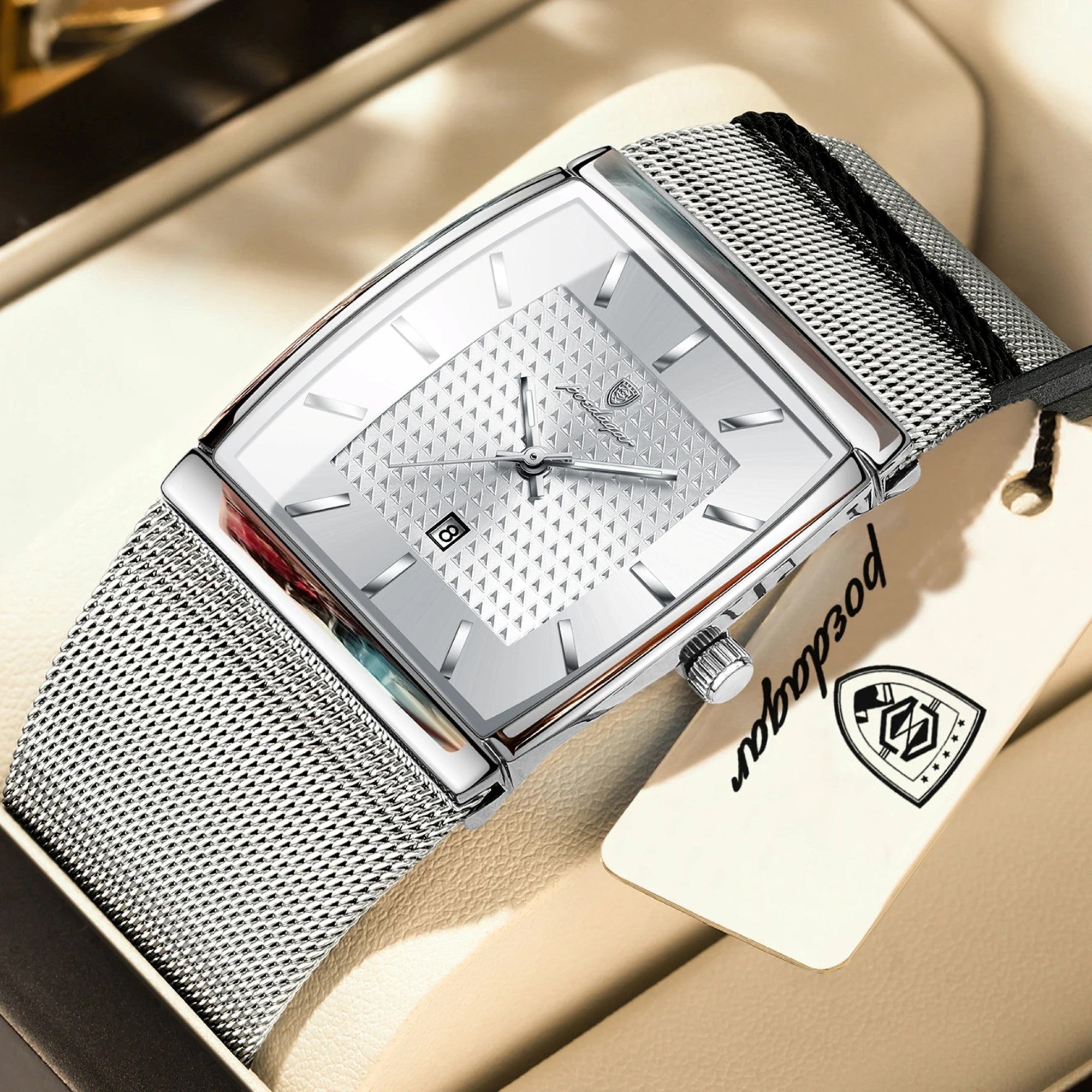 Silver watch with mesh band on a beige surface, brand tag visible
