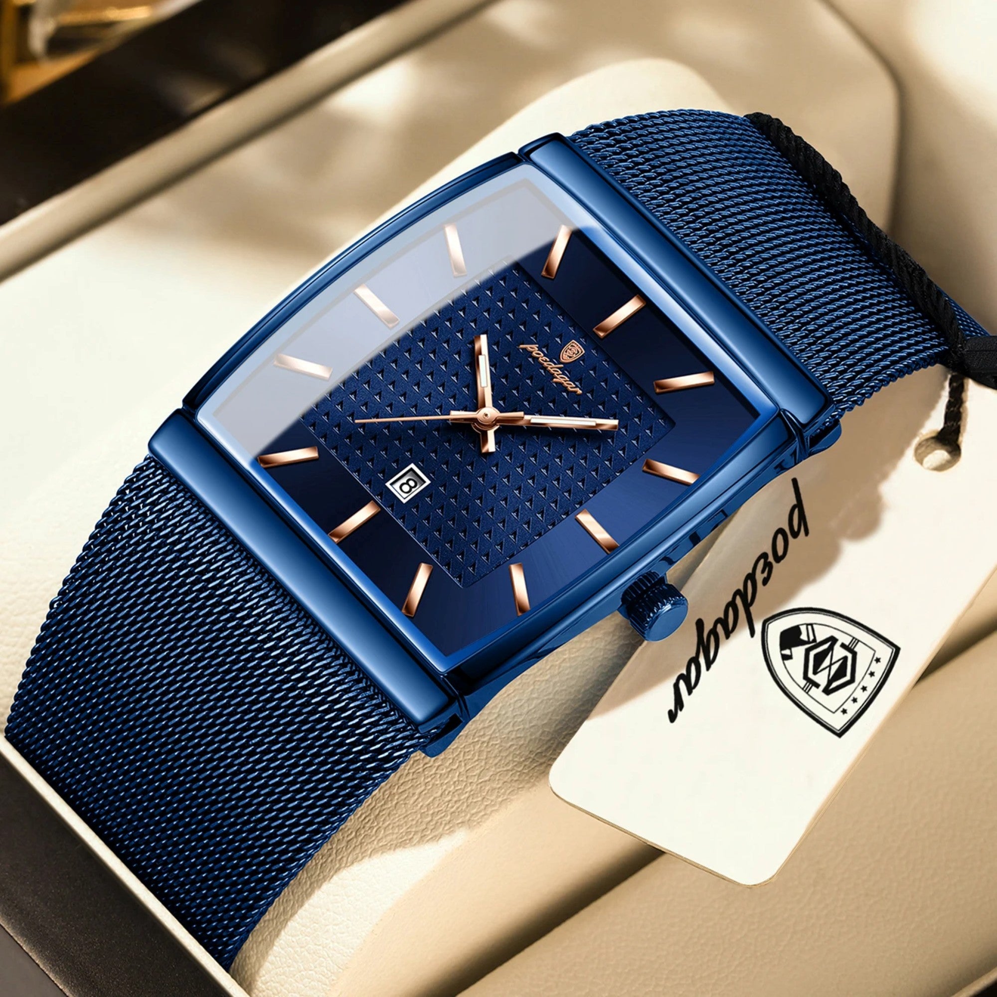 Blue watch with mesh band on a beige surface, featuring a brand tag.