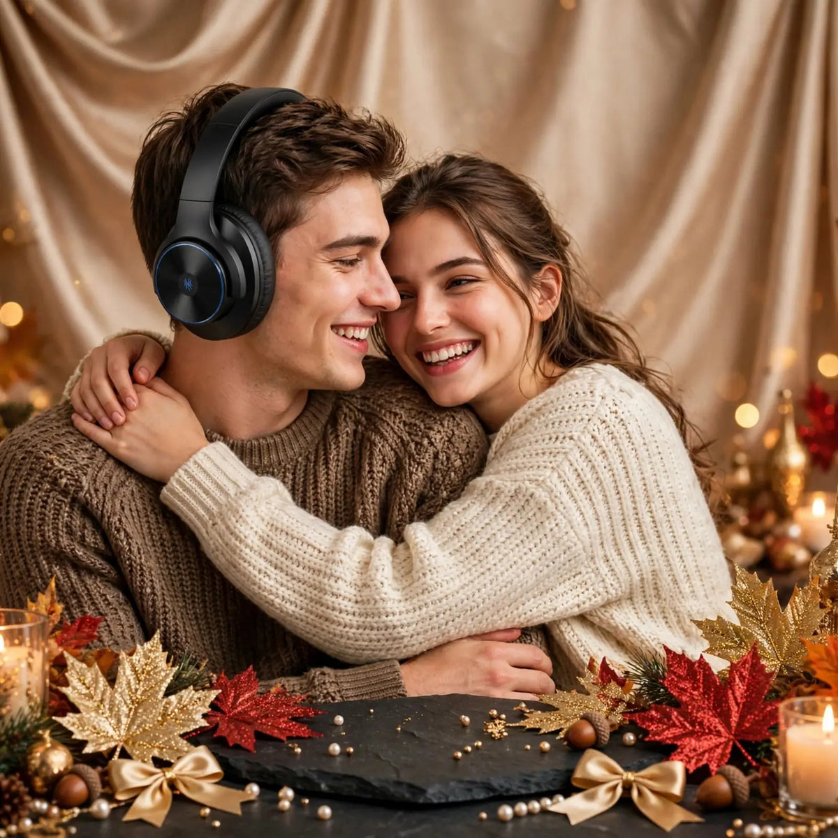 Happy couple hugging man wearing OneOdio A10 black headphones smiling at woman in cream sweater, champagne satin background, black slate with gold bows, glitter maple leaves, acorns, pearls and candles
