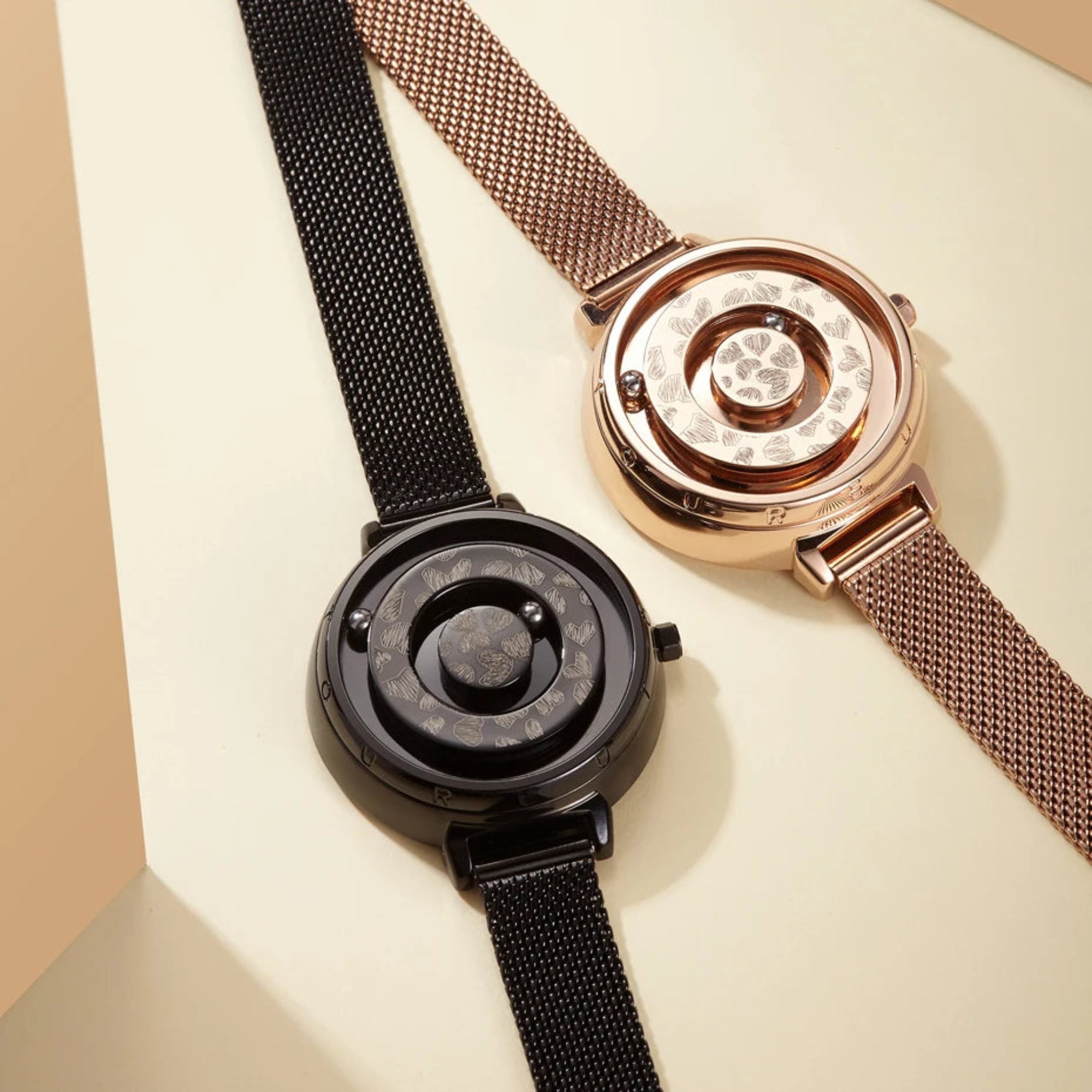 Two watches, one black and one rose gold, on a beige background
