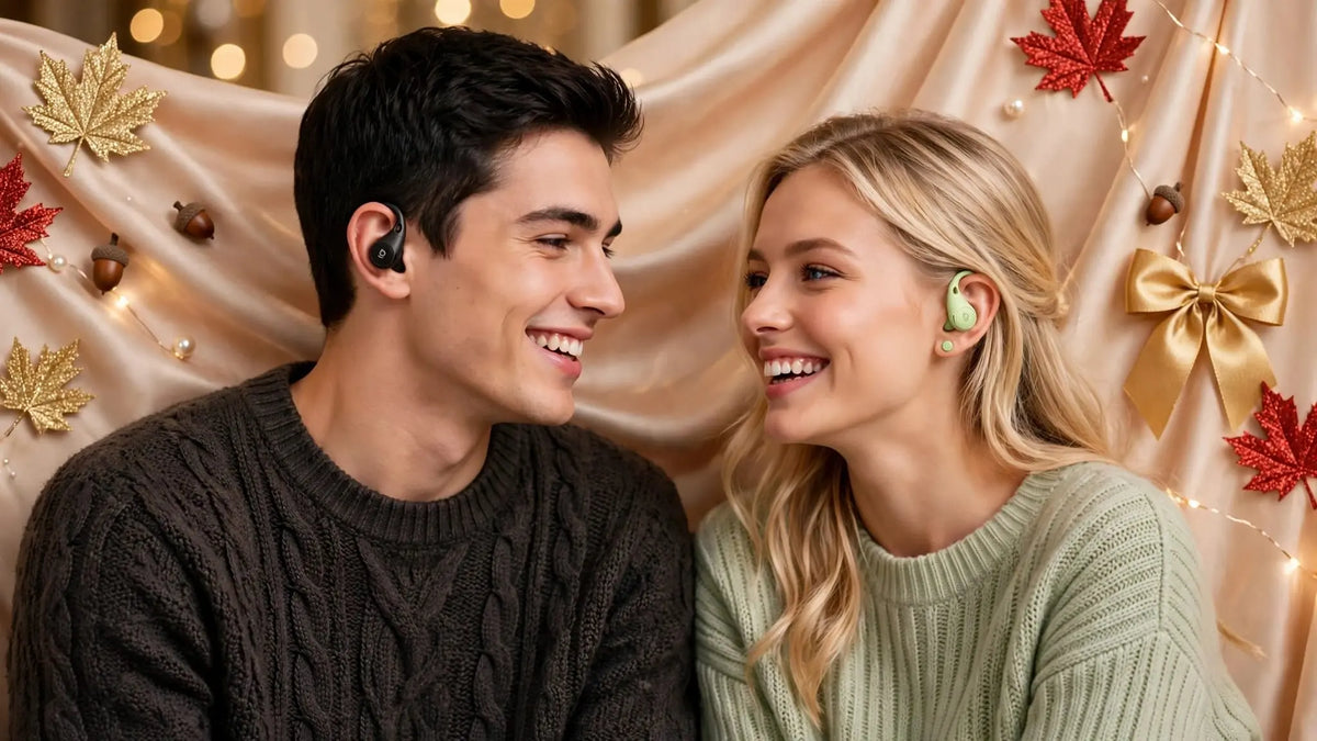 Young man wearing exact black open-ear earbuds and blonde woman wearing exact light green open-ear earbuds smiling at each other cozy autumn sweaters champagne silk background gold red glitter maple leaves acorns pearls gold satin bows fairy lights - luxury lifestyle banner no text Goldener Wahl