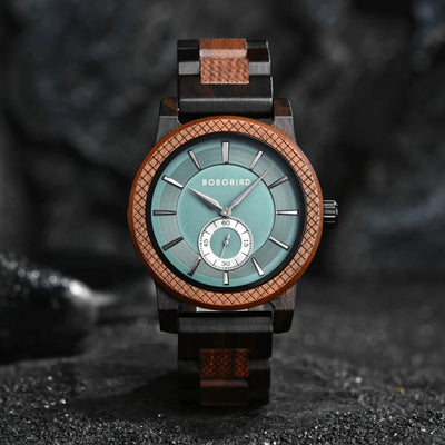 A wooden watch with a green dial and brown bands, displayed against a dark textured background with stones and a branch.