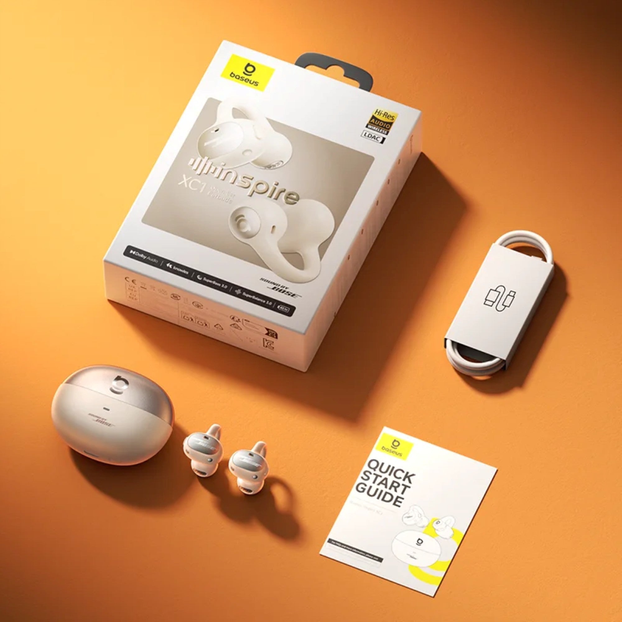 White wireless earbuds with packaging, earbud case, and quick start guide on an orange background