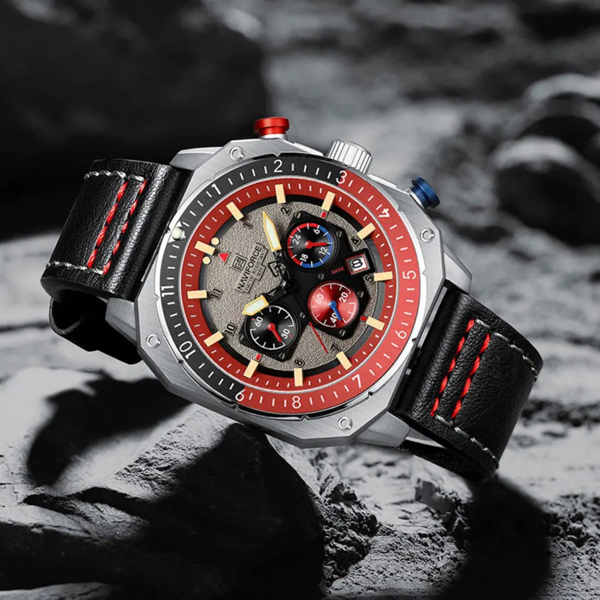 A wristwatch with a black leather band, silver metal case, red and gray dial, and red accents.