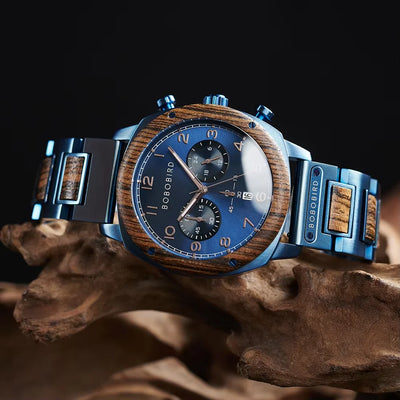 Boboibird wristwatch with a blue dial, blue-tone metal case and bracelet, and wood inlay details, displayed on a piece of driftwood against a dark background.