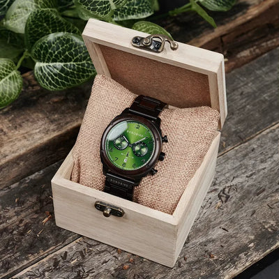 Green wristwatch in a wooden box on a rustic wooden surface with plants in the background