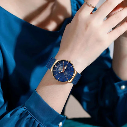 Hand wearing a blue watch with a matching blue dress against a neutral background