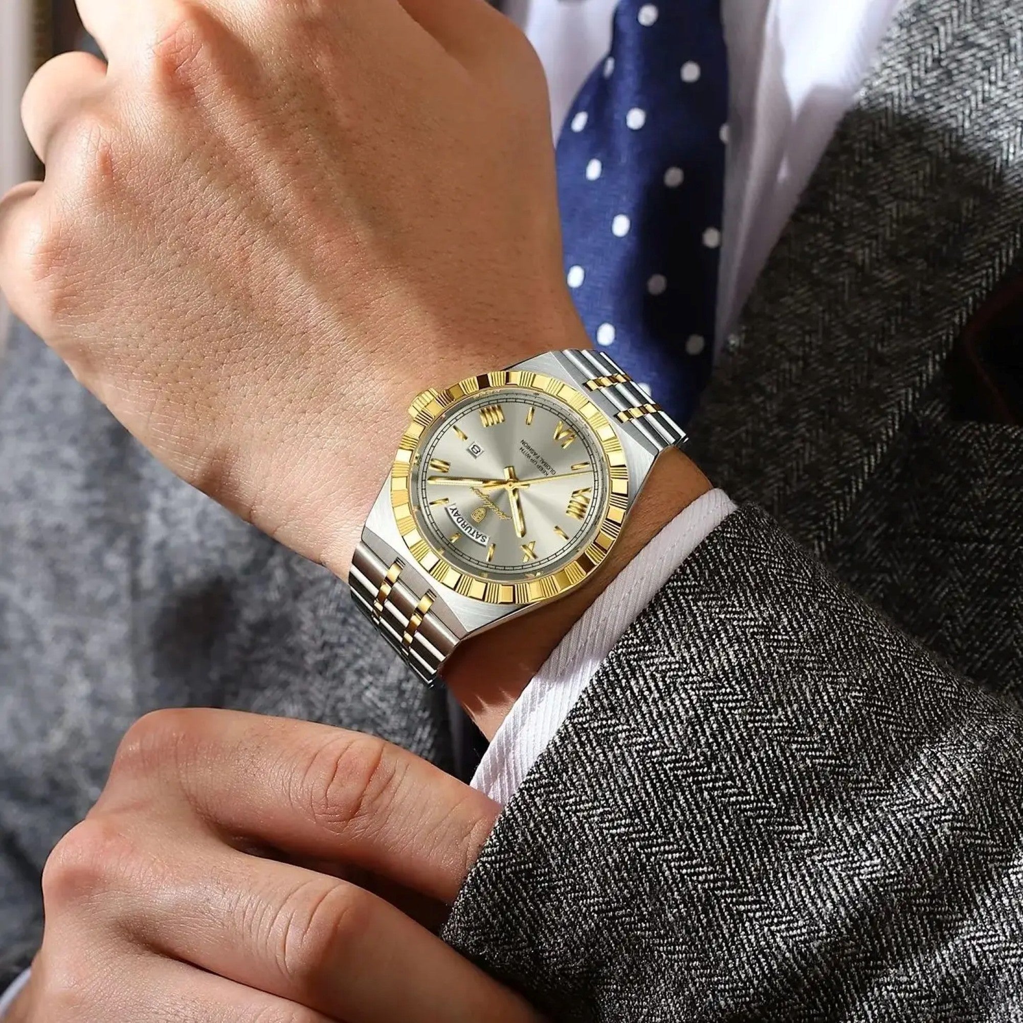 Close-up of a person wearing a gold and silver watch with a suit and tie in the background.