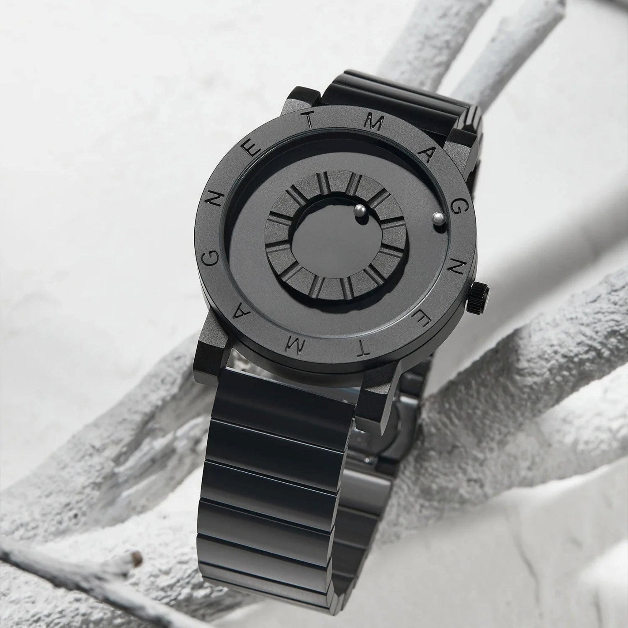 Black wristwatch with metallic band on a textured white surface