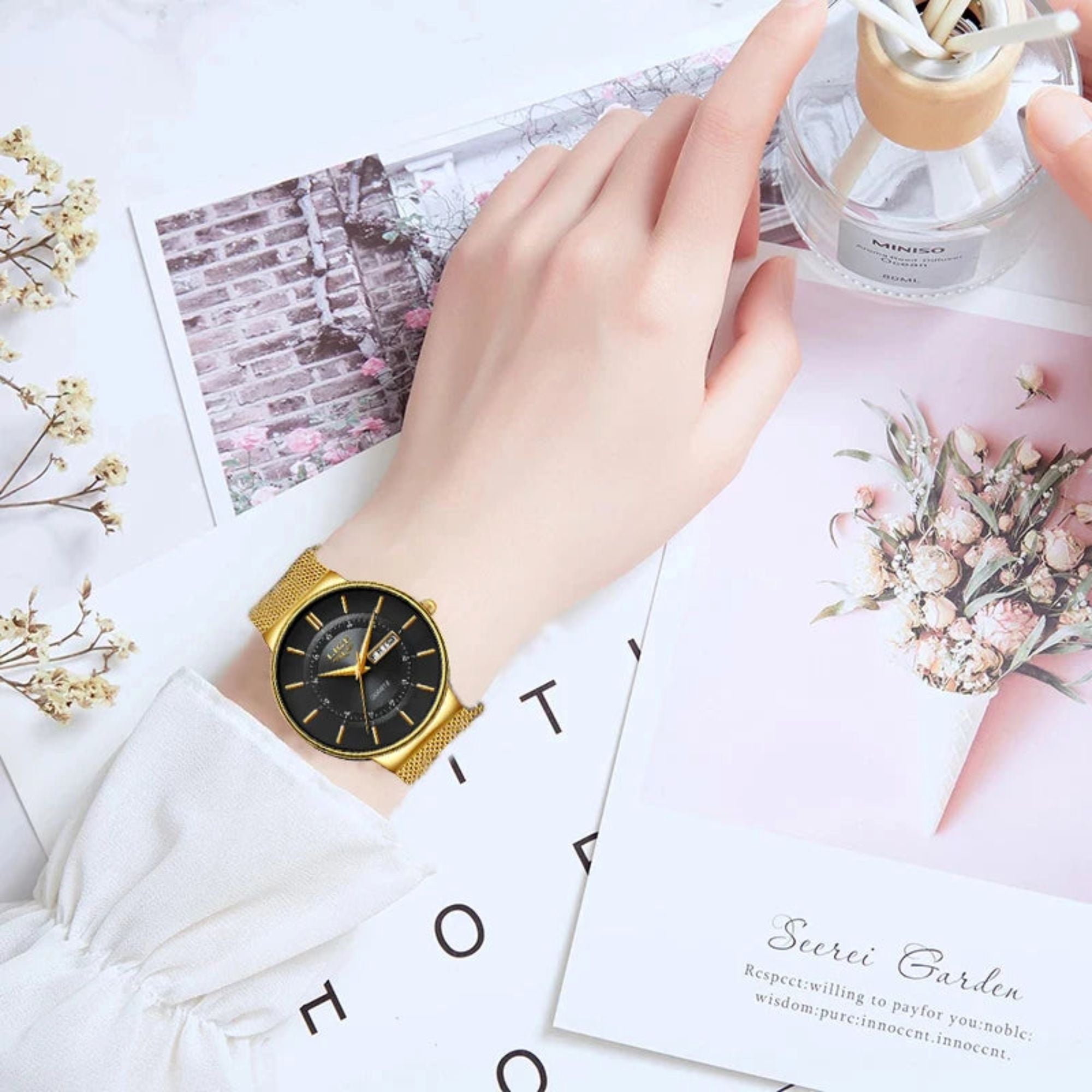 Gold watch on a wrist with a decorative background featuring flowers and cards.