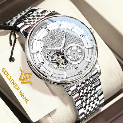 A luxury skeleton wristwatch with a silver stainless steel link bracelet and a detailed silver dial, presented inside its cream-colored gift box. A branded paper tag reading 'GOLDENER WAHL' is visible on the left.